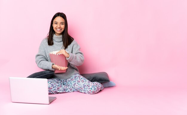 Jeune femme mangeant du pop-corn tout en regardant un film sur l'ordinateur portable holding copyspace imaginaire sur la paume pour insérer une annonce