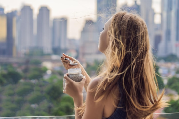 Jeune femme mangeant du pudding de chia sur son balcon donnant sur la grande ville