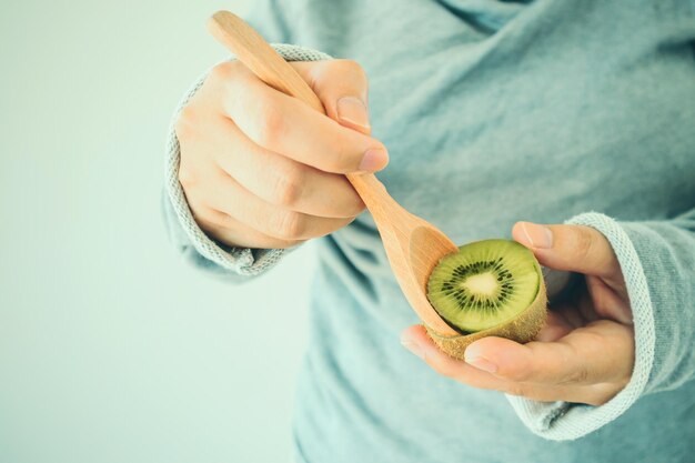 Jeune femme mangeant des kiwis mûrs avec une cuillère en bois