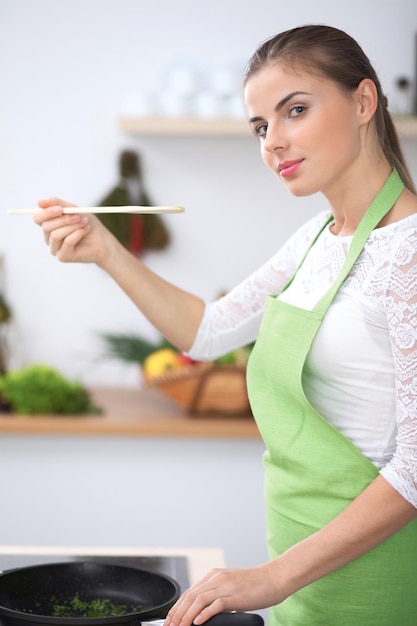 Jeune femme mangeant de la salade à la cuillère en bois pendant la cuisson dans une cuisine Repas sain et concept de travail de cuisine