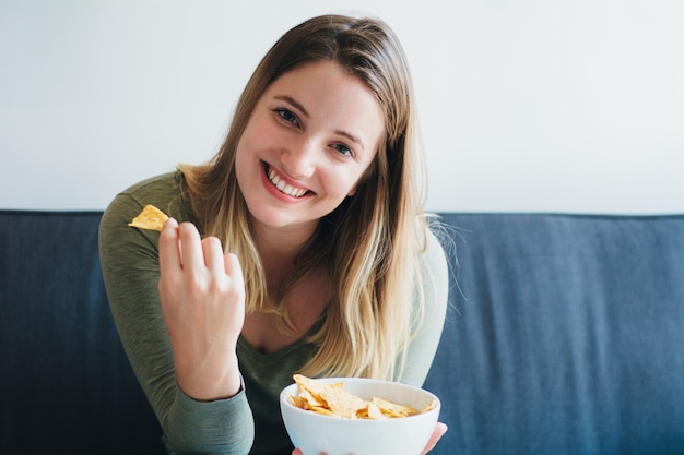 Jeune femme mangeant des snacks sur le canapé