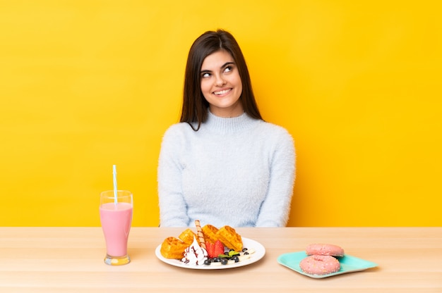 Jeune femme, manger, gaufres, et, milk-shake, dans, a, table, sur, isolé, mur jaune, rire, et, recherche