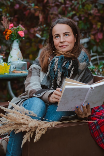 Jeune femme manteau brun siège chaise table livre de lecture avec plaid jeté sur sa tête