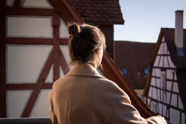 Jeune femme en manteau debout avec son dos sur fond de maisons