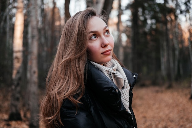 Jeune femme en manteau et écharpe debout dans la forêt d'automne sur fond d'arbres en plein air