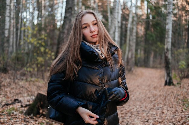 Jeune femme en manteau et écharpe debout dans la forêt d'automne en plein air