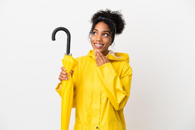 Jeune femme avec manteau imperméable et parapluie isolé sur fond blanc en levant tout en souriant