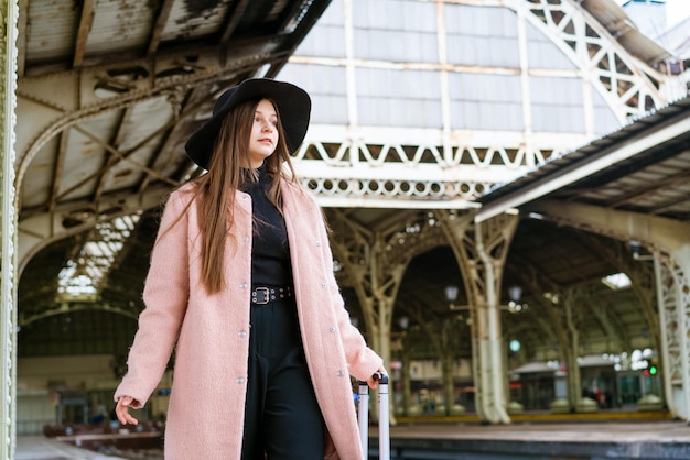 Jeune femme en manteau marche avec valise le long de la plate-forme vide de la gare caucasian girl touri...