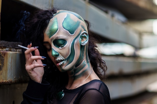 Jeune femme avec le maquillage du crâne vert pour la cigarette d'halloween.