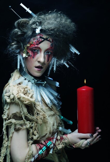 Jeune femme avec un maquillage lumineux portant un costume de carnaval tenant une bougie Photo d'Halloween