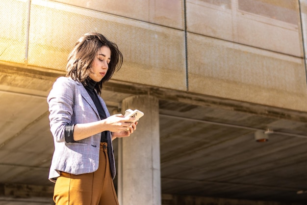 Jeune femme marchant dans la rue tenant un téléphone portable et un verre de café Une femme marchant dans la rue tenant un verre de café et utilisant un téléphone portable