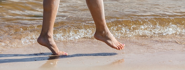 Jeune femme marchant le long de la plage de sable. Jambes féminines dans le sable au bord de la mer