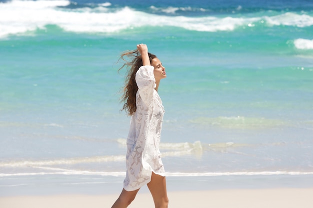 Jeune femme marchant sur la plage avec la main dans les cheveux