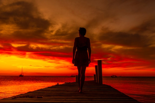 Une jeune femme marchant vers la mer au coucher du soleil sur la plage de West End à Roatan