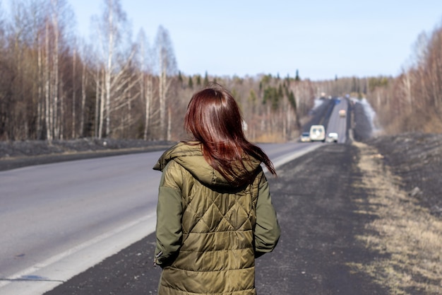 Une Jeune Femme Marche Sur Le Bord De La Route. Route Dans La Forêt.