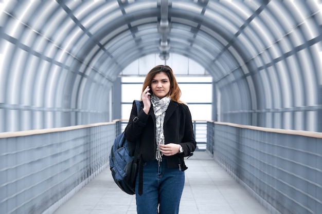 Une jeune femme marche rapidement le long d'un viaduc pour piétons couvert, parle au téléphone et sourit