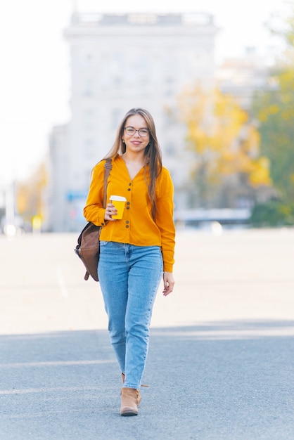 Une jeune femme marche avec une tasse de boisson chaude à la main