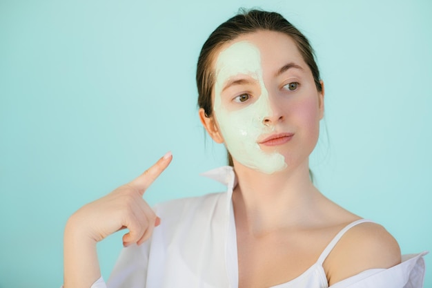 Jeune femme avec un masque d'argile sur son visage sur fond clair, espace pour le texte. Soin de la peau