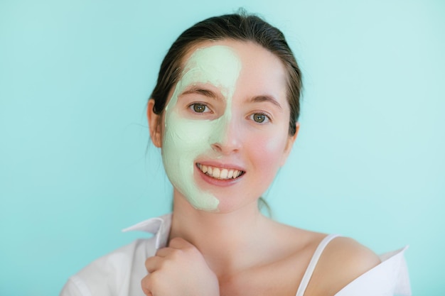 Jeune femme avec un masque d'argile sur son visage sur fond clair, espace pour le texte. Soin de la peau