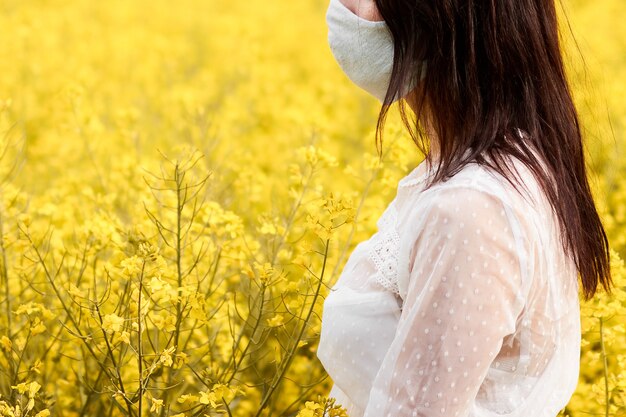 Jeune femme avec masque dans un champ avec des fleurs de viol