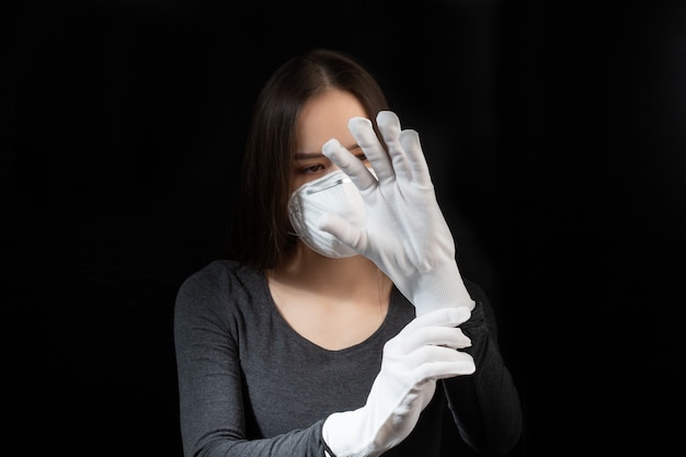 Jeune femme en masque médical antibactérien et gants sur un mur noir