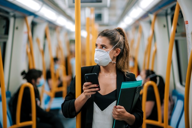 Jeune femme avec masque médical dans le métro utilise son téléphone