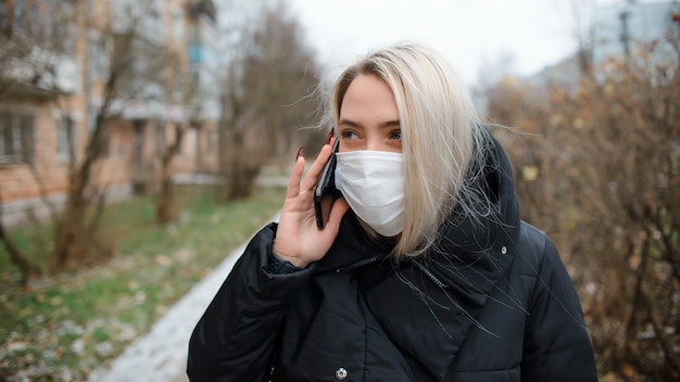 Jeune femme en masque médical, parler au téléphone à l'extérieur.