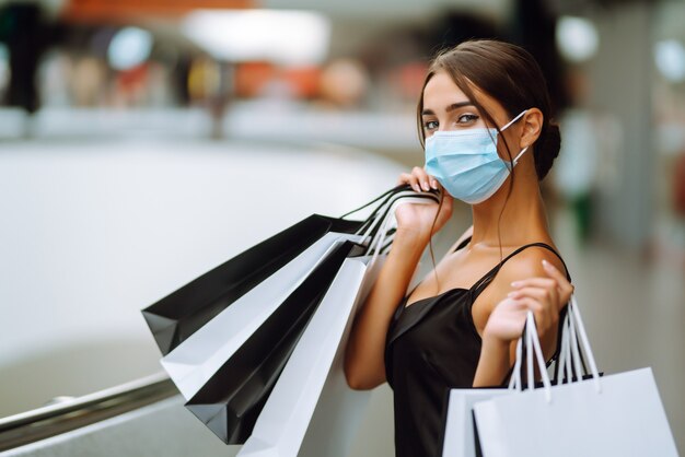 Jeune femme en masque médical stérile protecteur sur son visage avec des sacs à provisions dans le centre commercial.