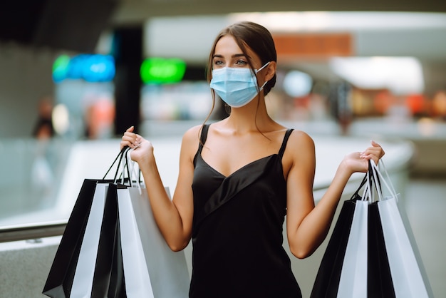 Jeune femme en masque médical stérile protecteur sur son visage avec des sacs à provisions dans le centre commercial.