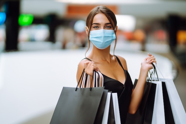 Jeune femme en masque médical stérile protecteur sur son visage avec des sacs à provisions dans le centre commercial.
