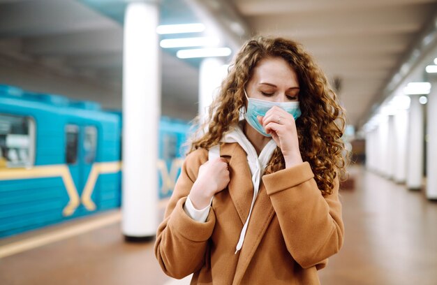 Jeune femme en masque médical stérile de protection toussant à la station de métro.