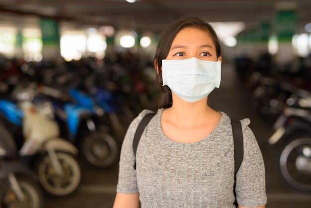 Jeune femme avec masque pensant sur le parking