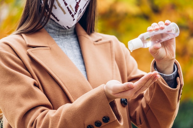 Jeune femme avec un masque de protection à l'aide d'un désinfectant