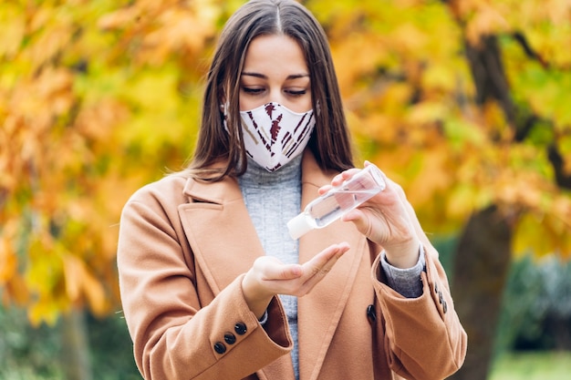 Photo jeune femme avec un masque de protection à l'aide d'un désinfectant