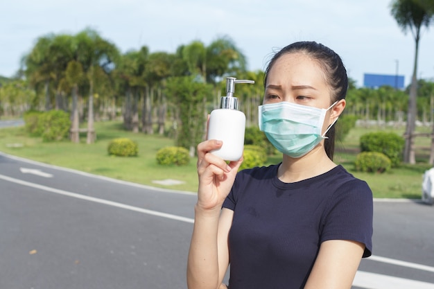 Jeune femme en masque de protection médicale et tenant un alcool à la main