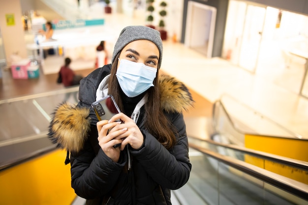 Jeune femme avec un masque de protection en prenant les escaliers dans un centre commercial