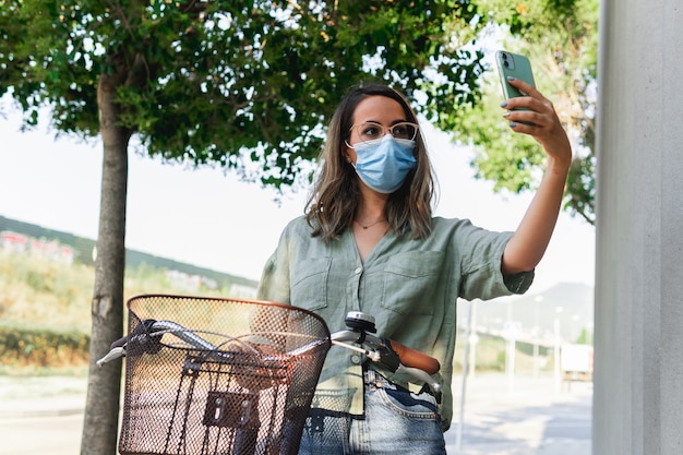 Jeune femme masquée faisant un selfie tout en tenant un vélo