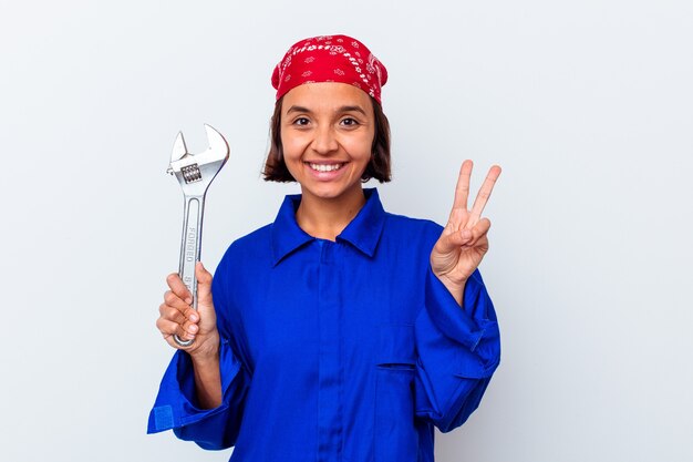 Jeune femme mécanique tenant une clé isolée joyeuse et insouciante montrant un symbole de paix avec les doigts.