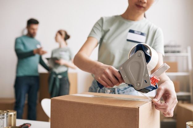 Jeune femme méconnaissable emballant des boîtes lors d'un événement caritatif et de dons, espace de copie