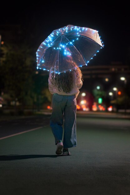 Jeune femme méconnaissable marchant avec un parapluie avec des lumières la nuit