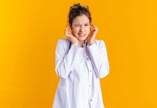 Jeune femme mécontente en uniforme de médecin avec stéthoscope fermant les oreilles