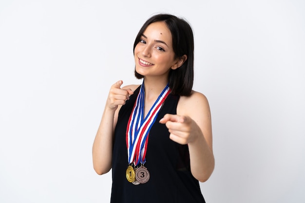 Jeune femme avec des médailles isolé sur un mur blanc pointe du doigt vers vous avec une expression confiante