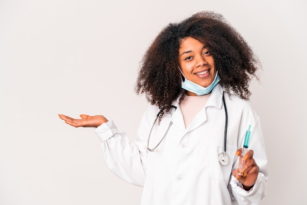 Jeune femme médecin afro-américaine bouclés tenant une seringue montrant un espace de copie sur une paume et tenant une autre main sur la taille.