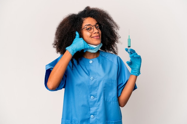 Jeune femme médecin afro-américaine bouclés tenant une seringue montrant un geste d'appel de téléphone mobile avec les doigts.