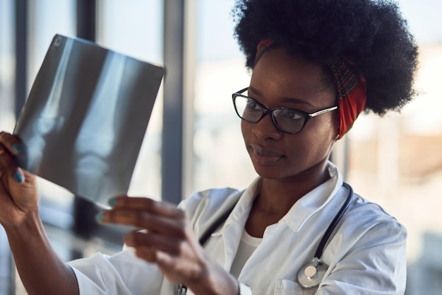 Une jeune femme médecin afro-américaine en uniforme blanc regarde les rayons X.