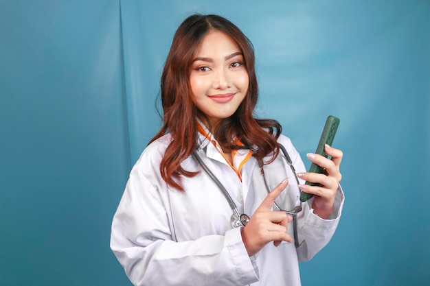 Une jeune femme médecin asiatique pointe et montre un écran vert ou un espace de copie sur son smartphone