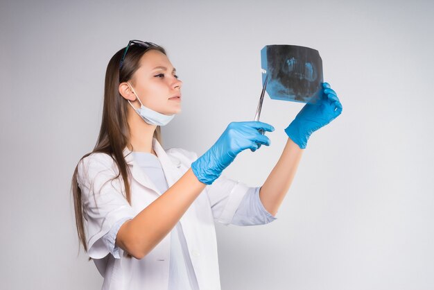 Une jeune femme médecin en blouse blanche portant des gants bleus examine une radiographie