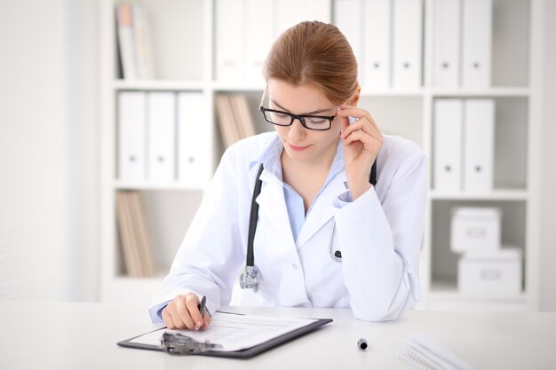 Jeune femme médecin brune assise à la table et travaillant au bureau de l'hôpital. Concept de soins de santé, d'assurance et d'aide. Médecin prêt à examiner le patient