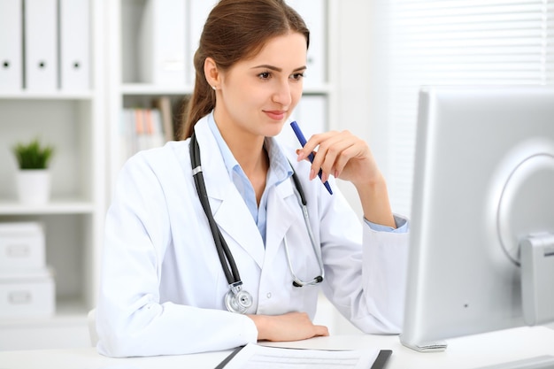 Jeune femme médecin brune assise à la table et travaillant au bureau de l'hôpital