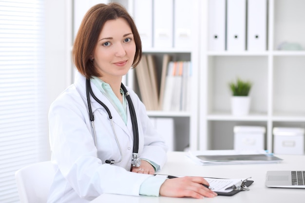 Jeune femme médecin brune assise à la table et travaillant au bureau de l'hôpital